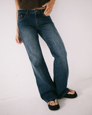 Woman wearing Shorty Freida Flare Low Rise Jeans in Blasted Deep Sea Blue