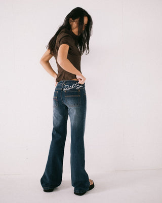 Woman wearing Shorty Freida Flare Low Rise Jeans in Blasted Deep Sea Blue